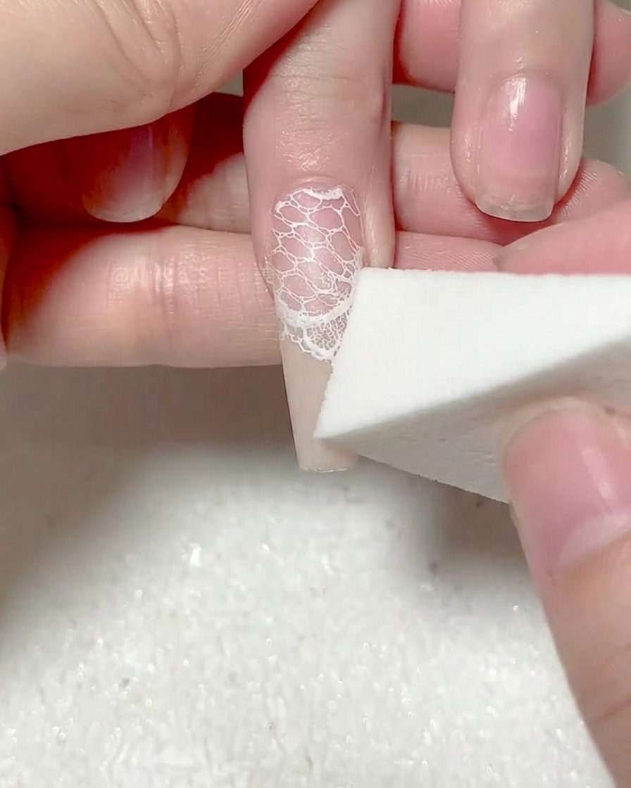 Una esponja de maquillaje dando toques a una segunda capa de gel blanco en la punta de la uña.