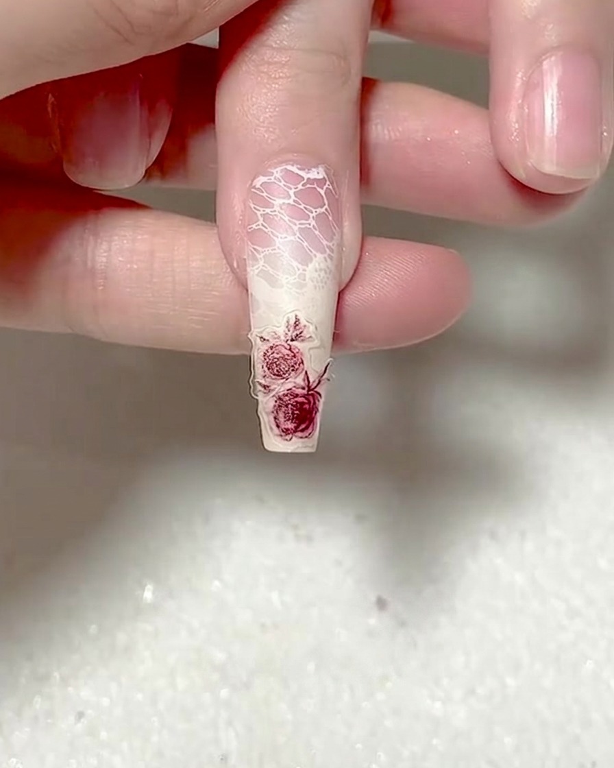 Una herramienta con punta de silicona presionando firmemente sobre un adhesivo de uña de rosa roja.