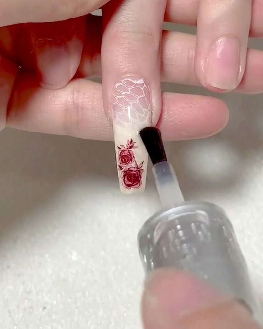 Un pincel aplicando gel base transparente sobre un adhesivo de rosa para encapsularlo.