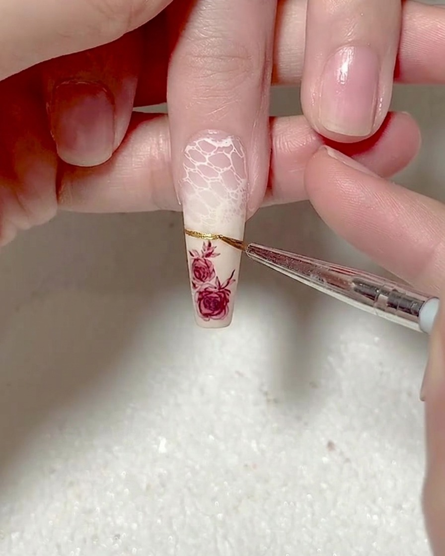 Primer plano de un pincel liner aplicando una línea de punta francesa de gel metálico dorado precisa a través de una uña.