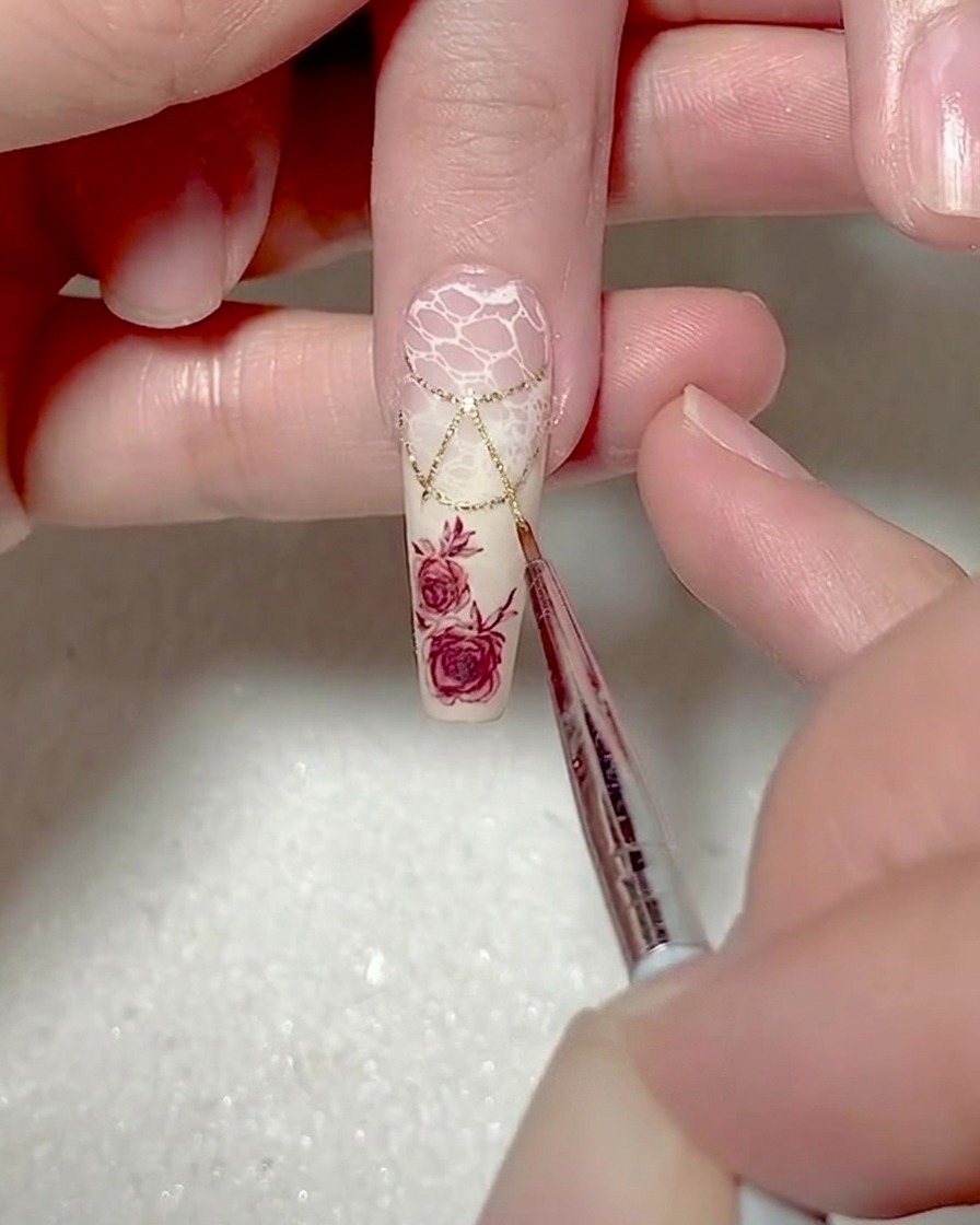 Primer plano de un pincel liner fino añadiendo contornos de gel blanco a lo largo de los bordes de un diseño de triángulo en una uña.