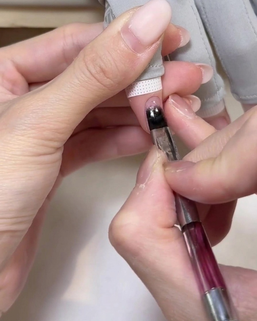 Una mano colocada dentro de una lámpara UV portátil, con las uñas recibiendo luz para curar el gel base.