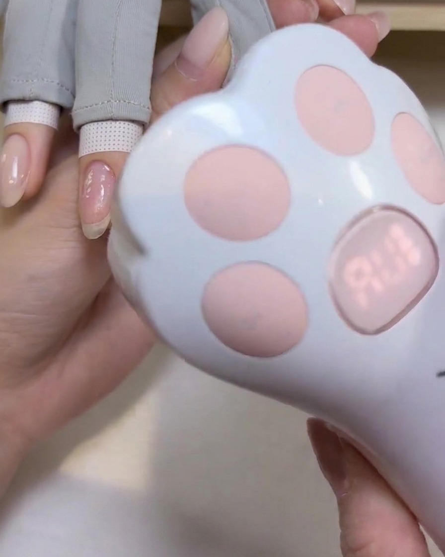 Una lámpara UV/LED portátil con forma de pata de gato colocada sobre una uña para curar el esmalte de gel.