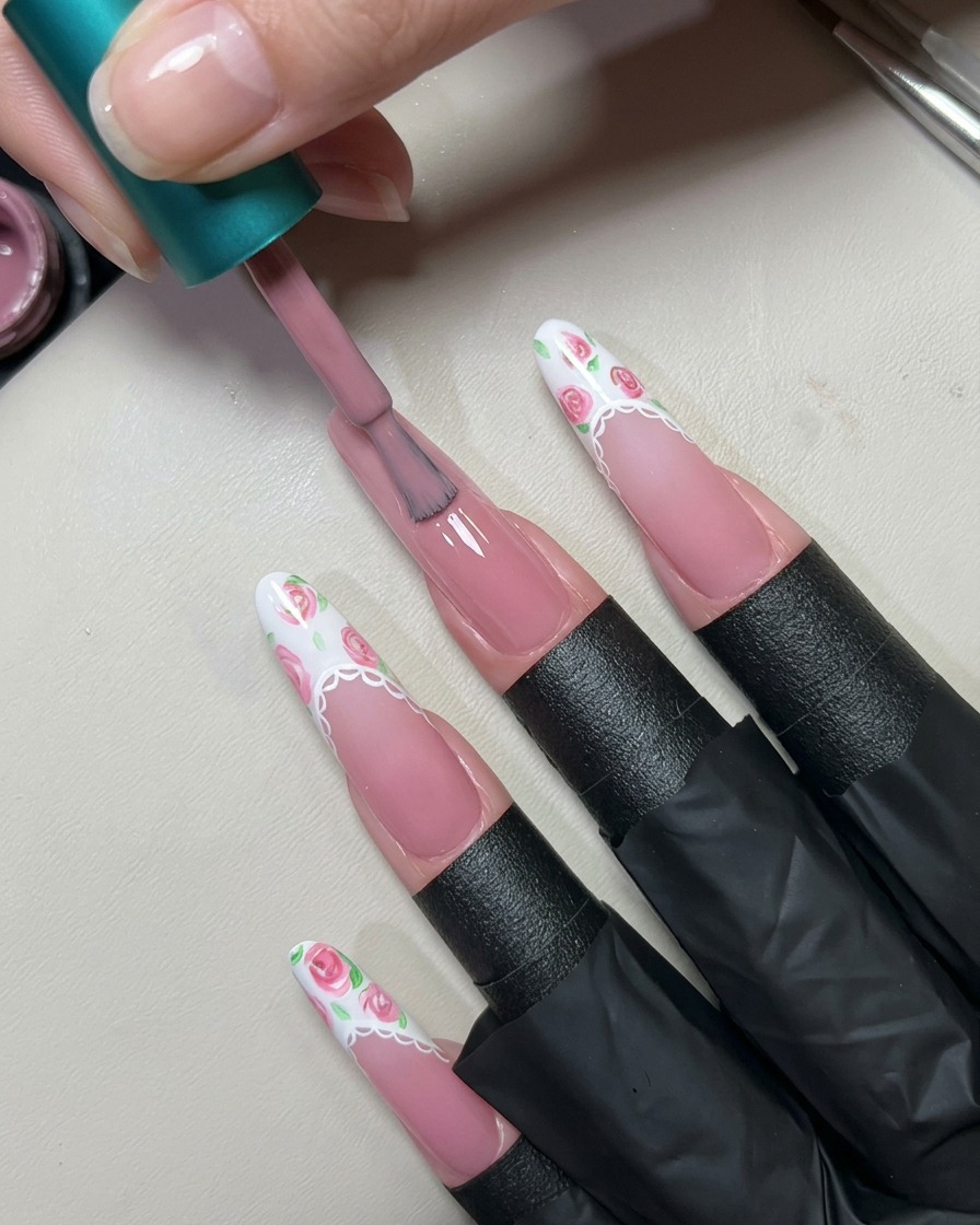 Un pincel aplicando una capa de gel rosa nude translúcido sobre una uña larga preparada.