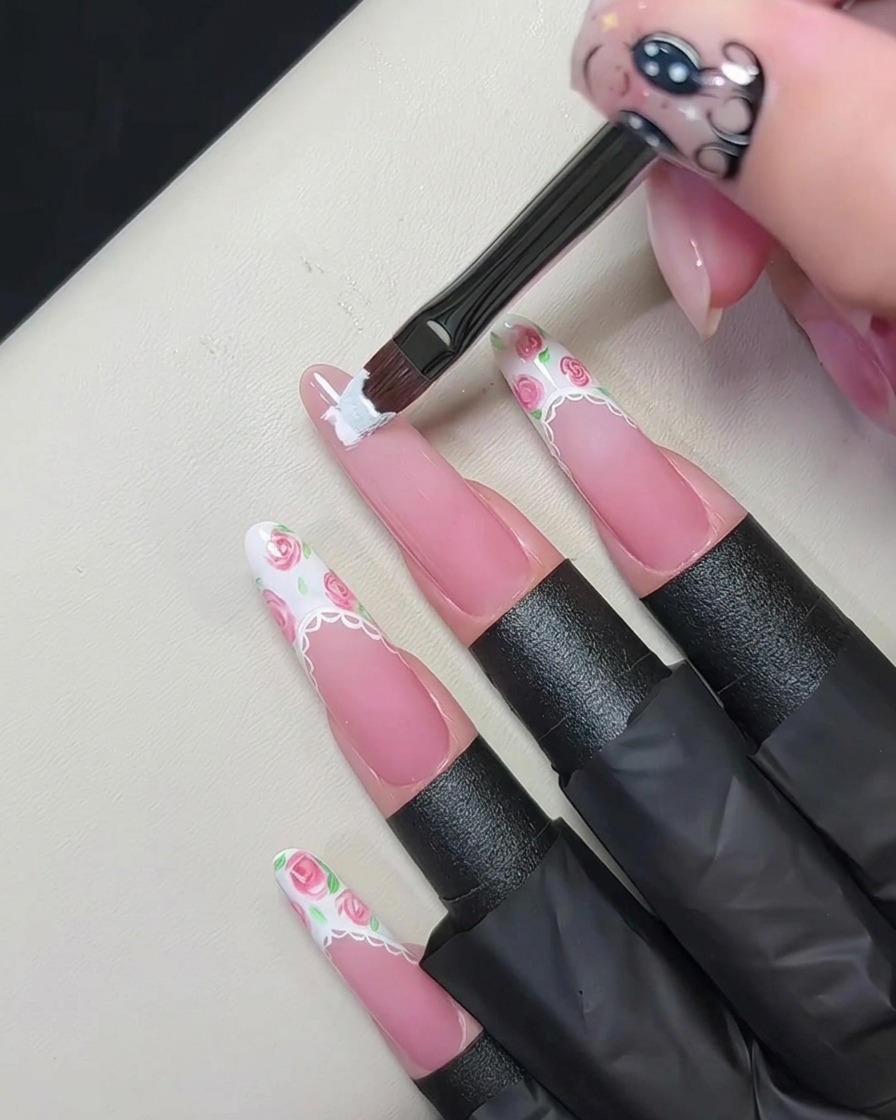 Un pincel de gel plano aplicando una punta francesa blanca gruesa en el borde de una uña rosa nude.
