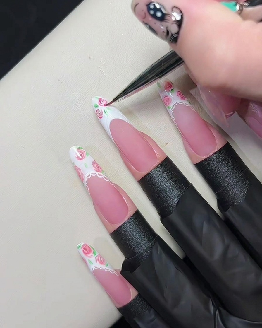 Un pincel de detalle fino mezclando gel rosa sobre el gel blanco húmedo en una punta francesa para crear patrones de rosas diminutas.