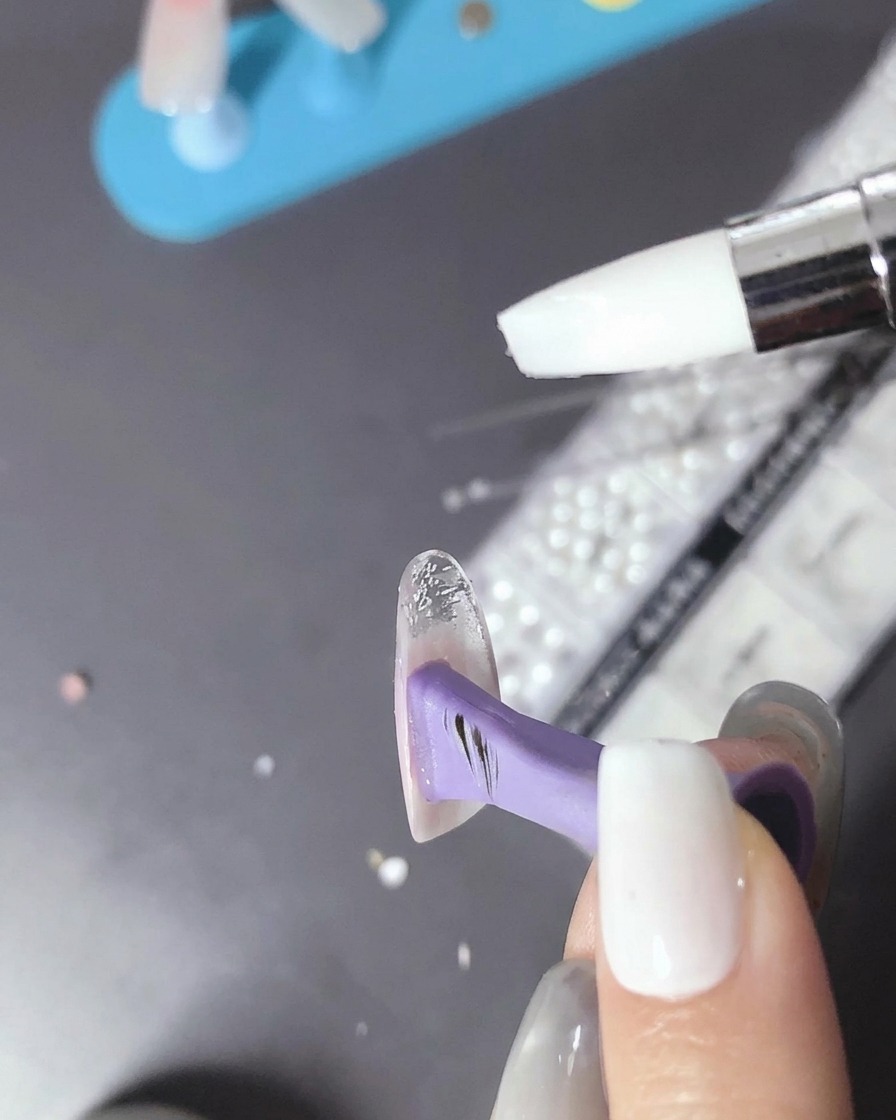 Un pincel aplicando una gota de gel transparente sobre la uña curada.