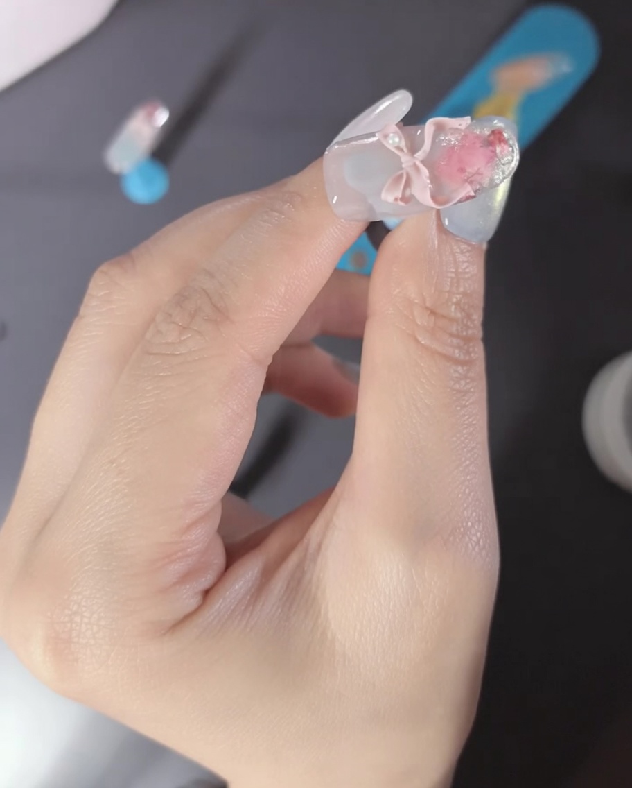 Primer plano de un dedo con un lazo 3D rosa y detalles de perlas.