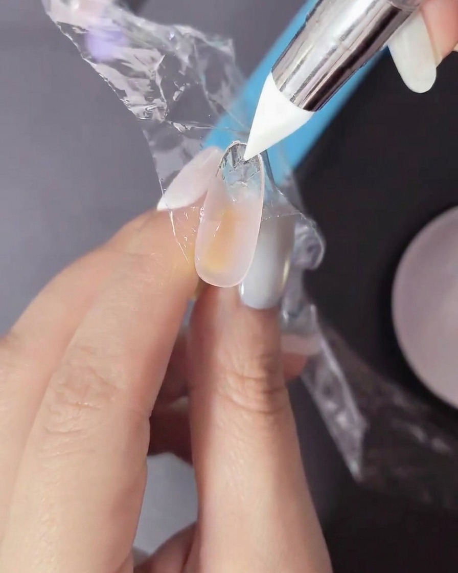 Un dedo con gel sin curar siendo presionado con un film plástico y una herramienta de silicona.