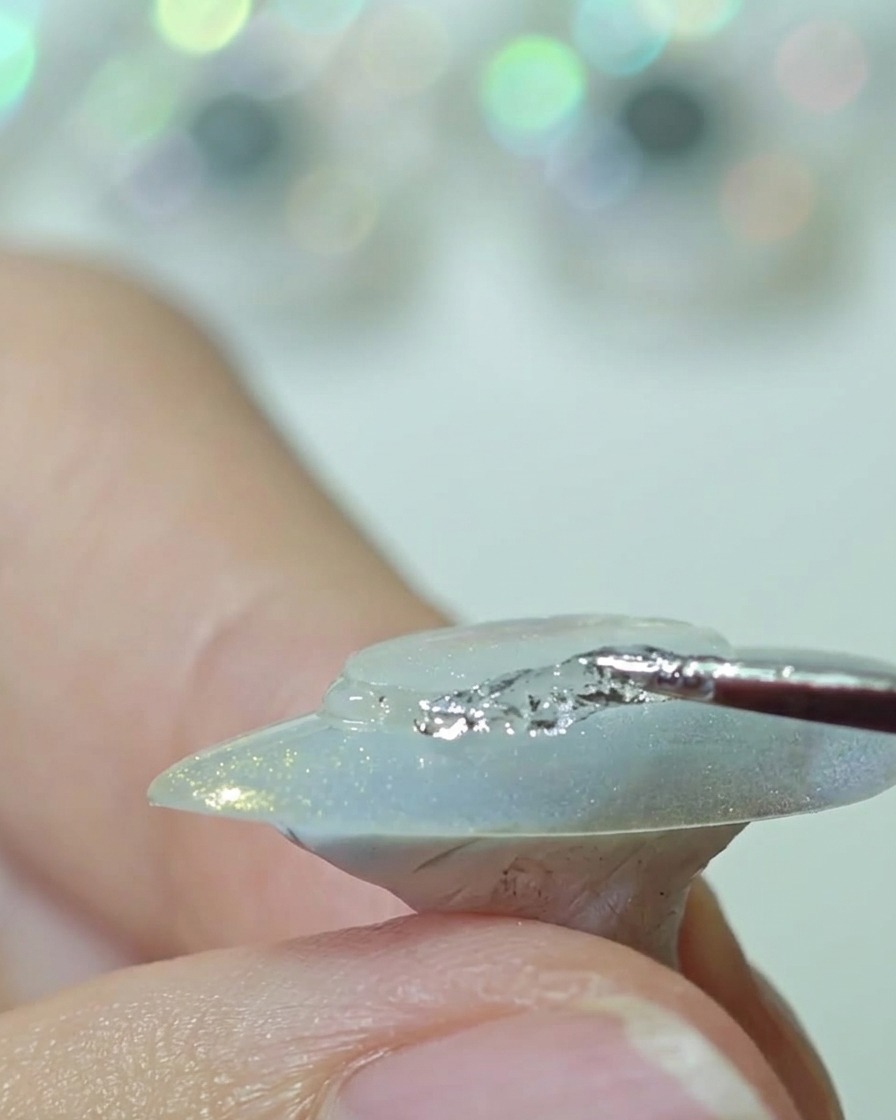 Una herramienta de silicona presionando un disco de plástico transparente sobre el centro de una uña, alisando los bordes.