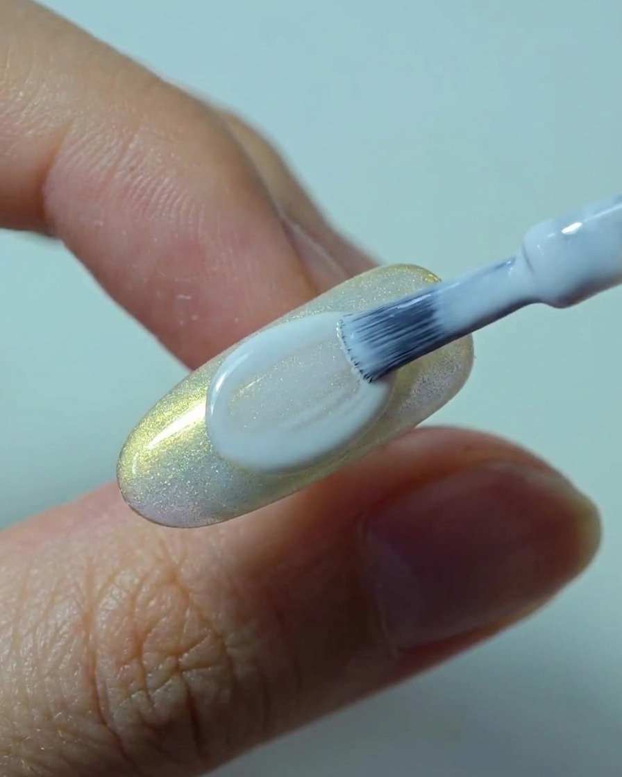 Un pincel aplicando una segunda capa suave y opaca de esmalte en gel blanco sobre la uña.