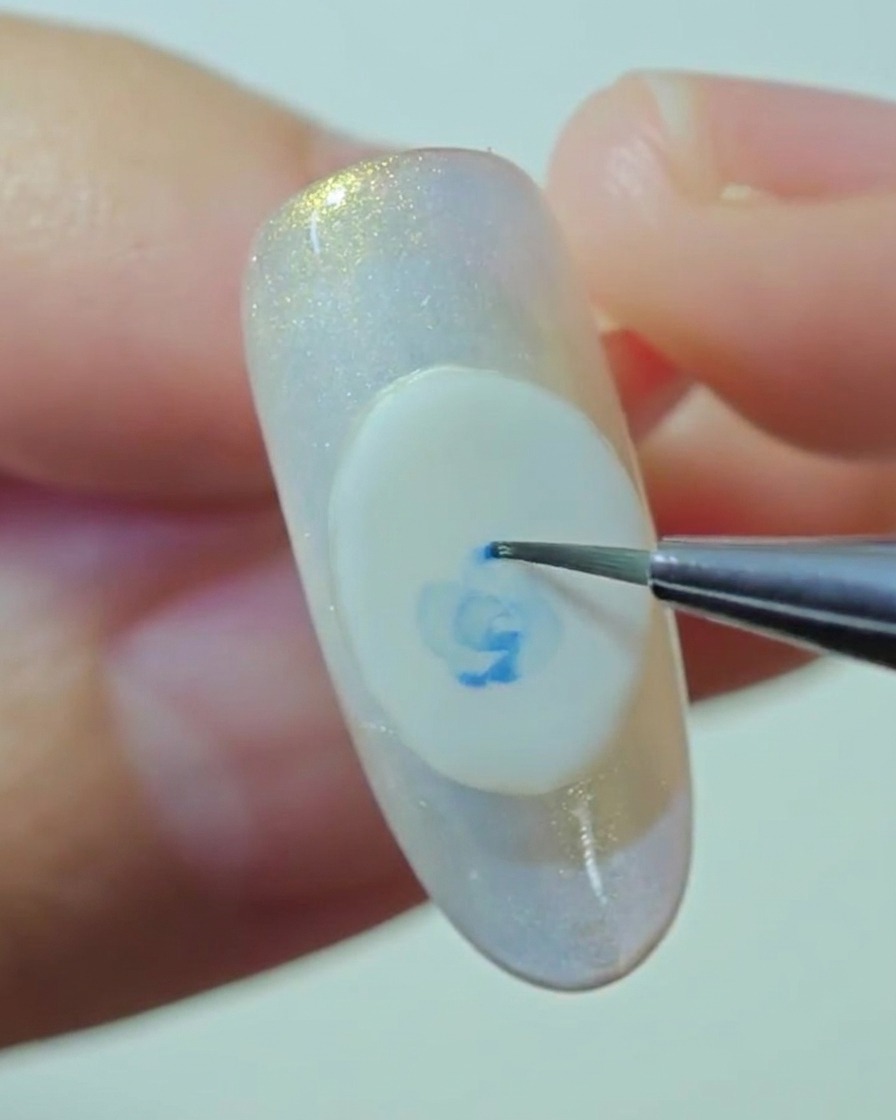 Una vista en primer plano de un pincel de detalle difuminando suavemente los bordes de una rosa azul pintada sobre una base de gel blanco.