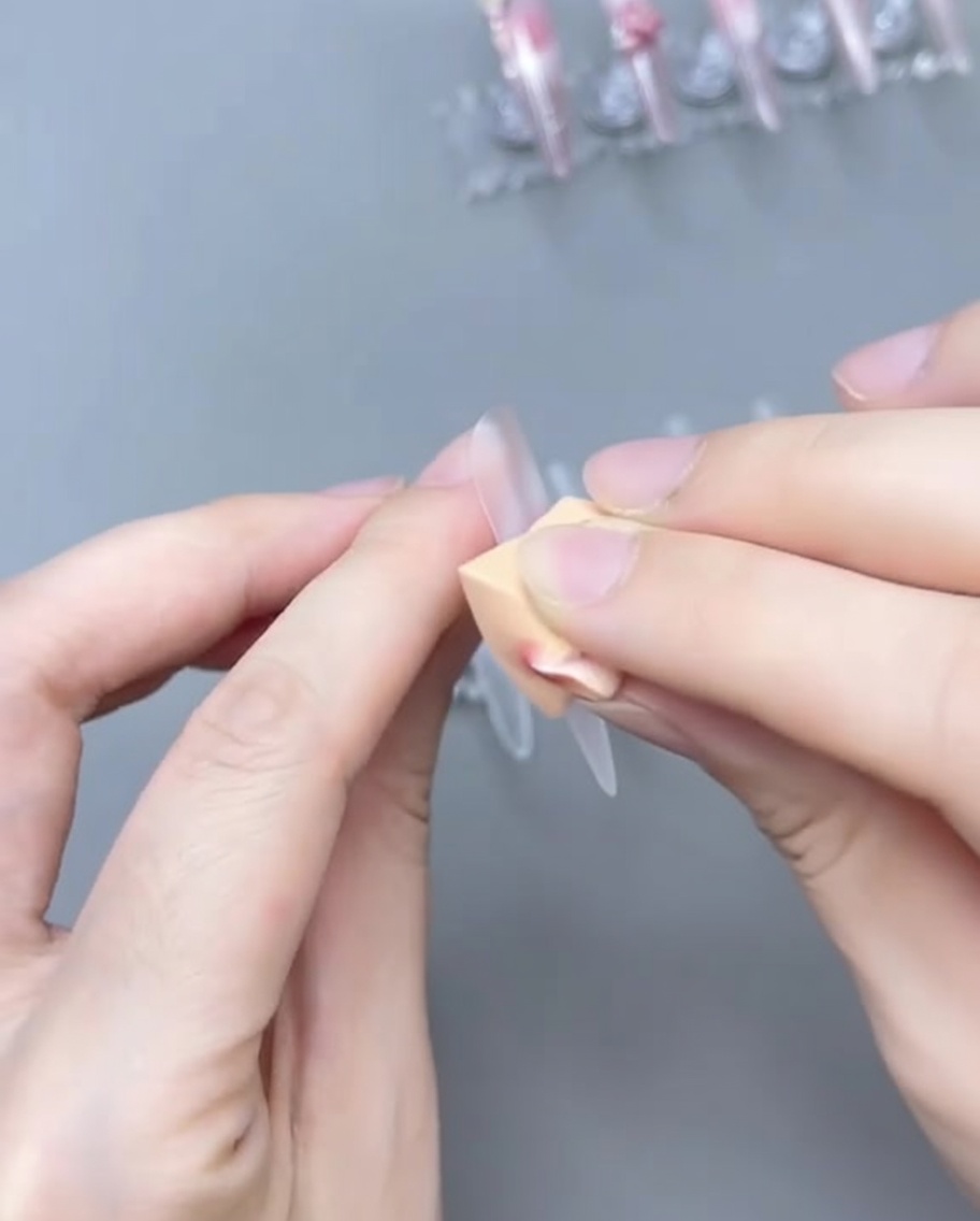 Un pincel difuminando gel rosa translúcido en el tip de la uña para crear un degradado ombré.