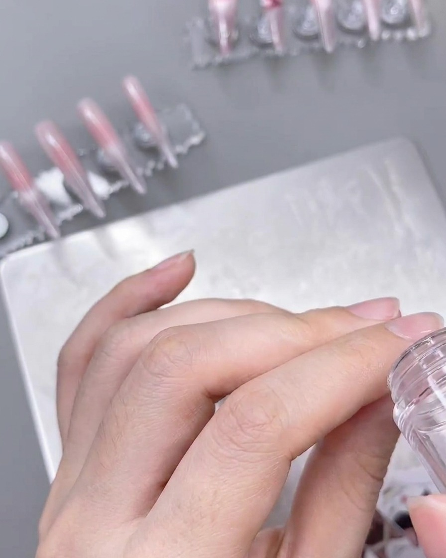 Un estampador transparente aplicando un delicado patrón de encaje blanco sobre una uña preparada con color ombré.