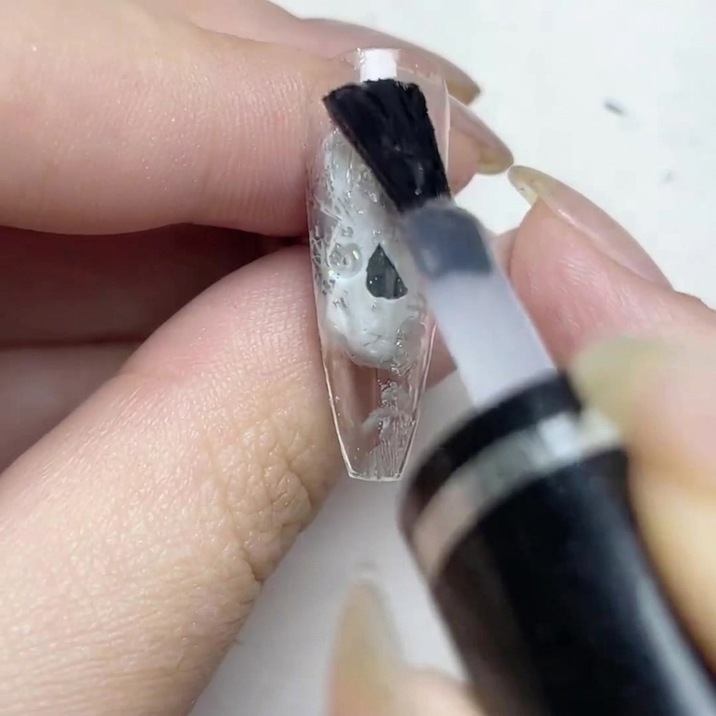 Un pincel aplicando una capa de top coat mate sobre la uña con lámina plateada.