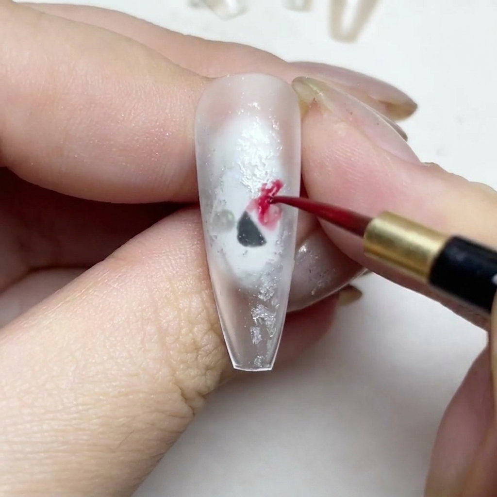 Un pincel fino de detalle pintando pétalos de rosa en acuarela roja sobre una uña.