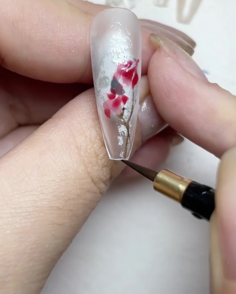 Dibujando finos tallos y hojas marrones y verdes alrededor del diseño de rosa.