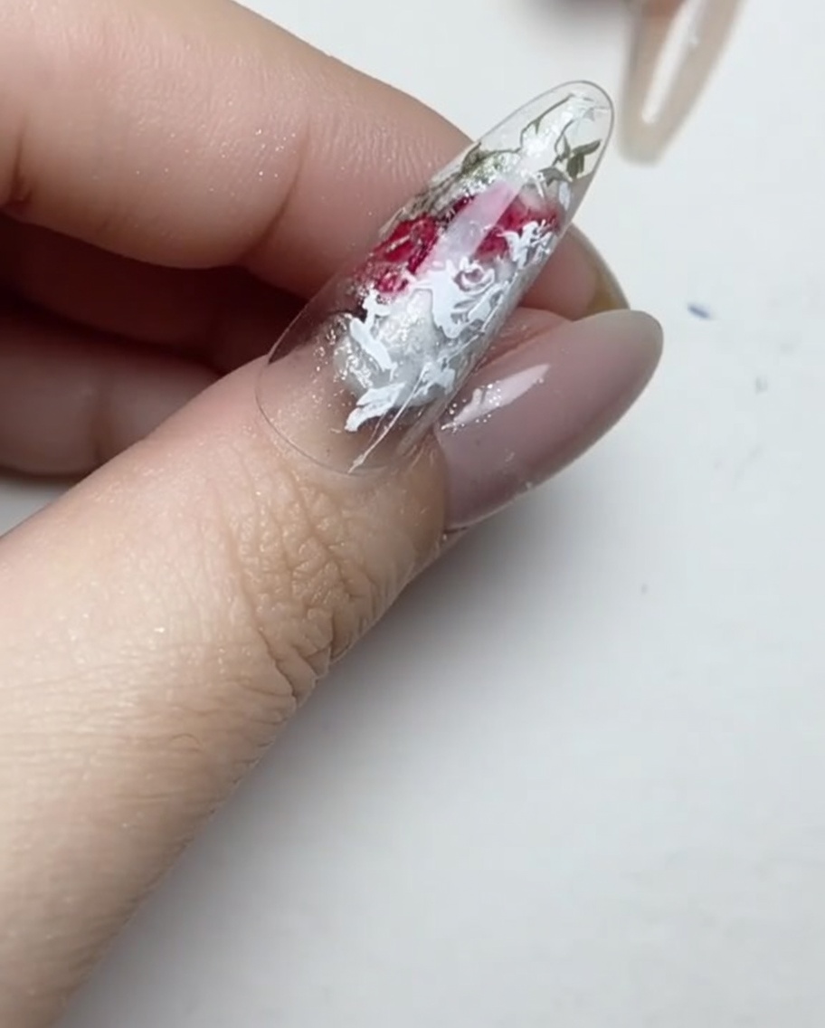 Un pincel delineador aplicando pequeñas gotas transparentes de adhesivo de gel sobre la superficie de una uña manicurada.