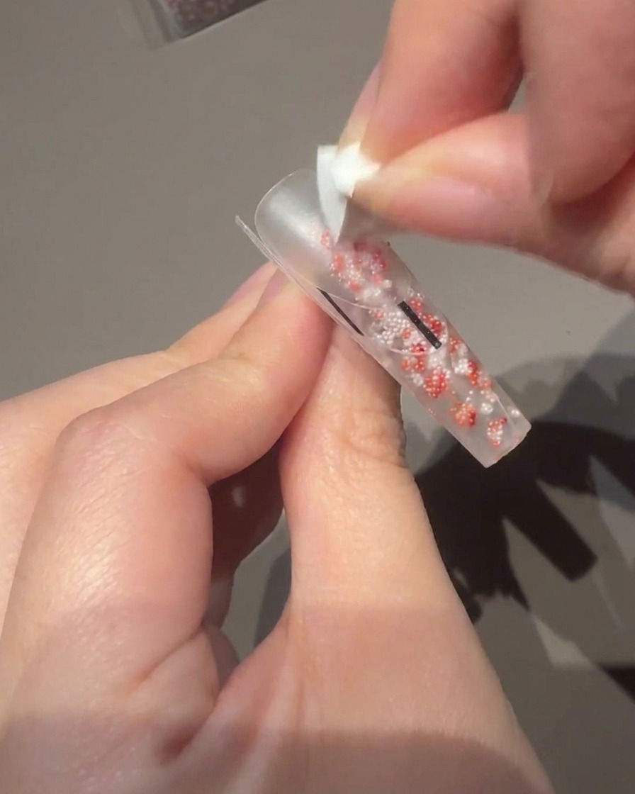 Usando un pequeño pincel para gel para aplicar un esmalte rosa lechoso sobre la base de la uña.