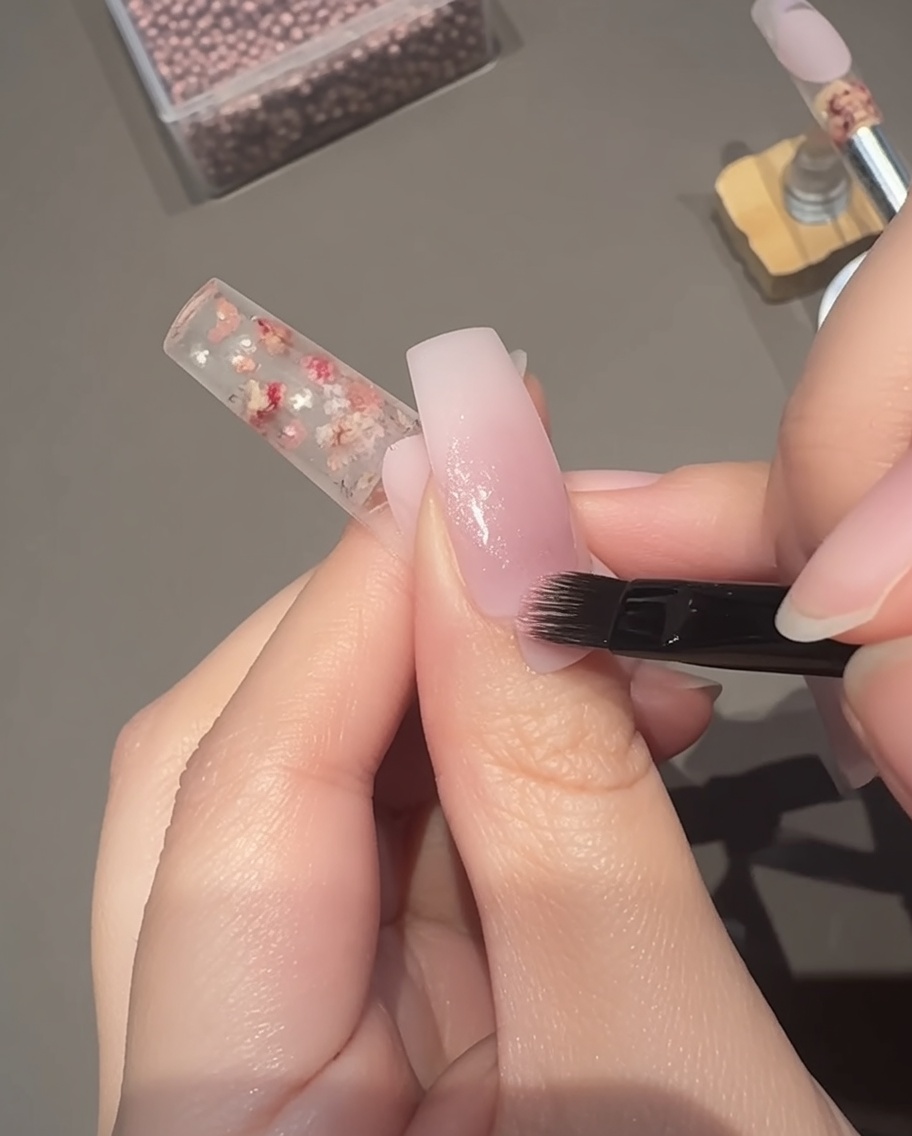 Aplicando un gel rosa transparente magnético ojo de gato sobre la base de la uña con un pincel.
