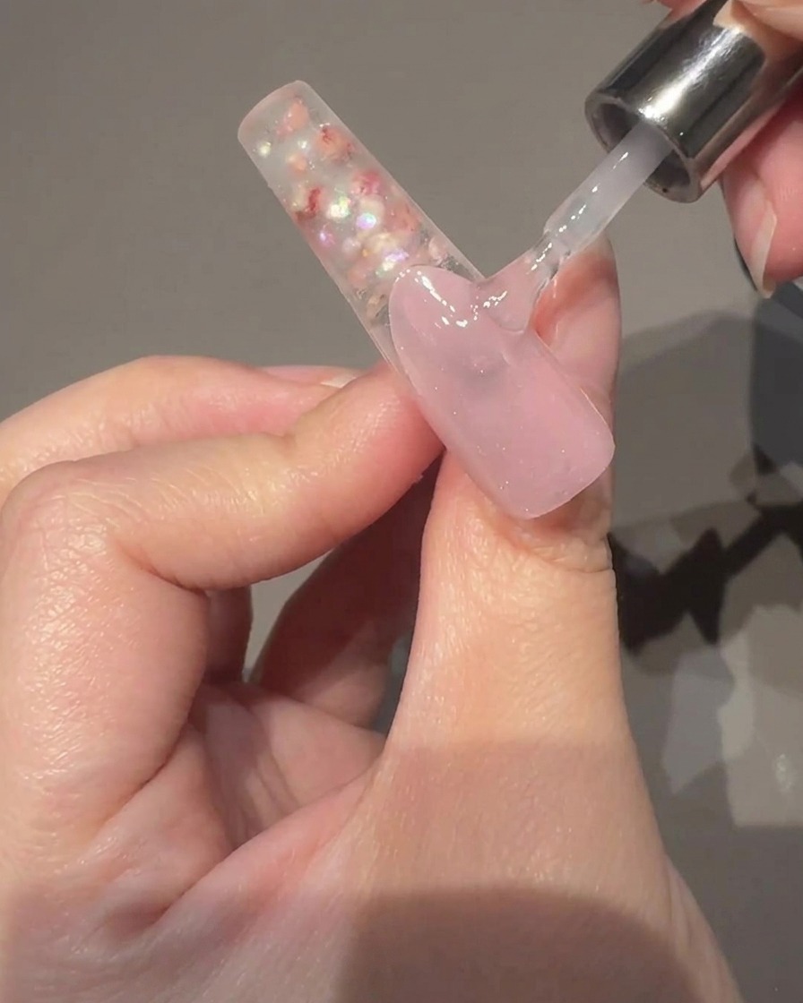 Un primer plano de una mano sosteniendo una varita magnética junto a una uña cubierta de gel ojo de gato húmedo, mostrando el brillo moviéndose hacia el centro.