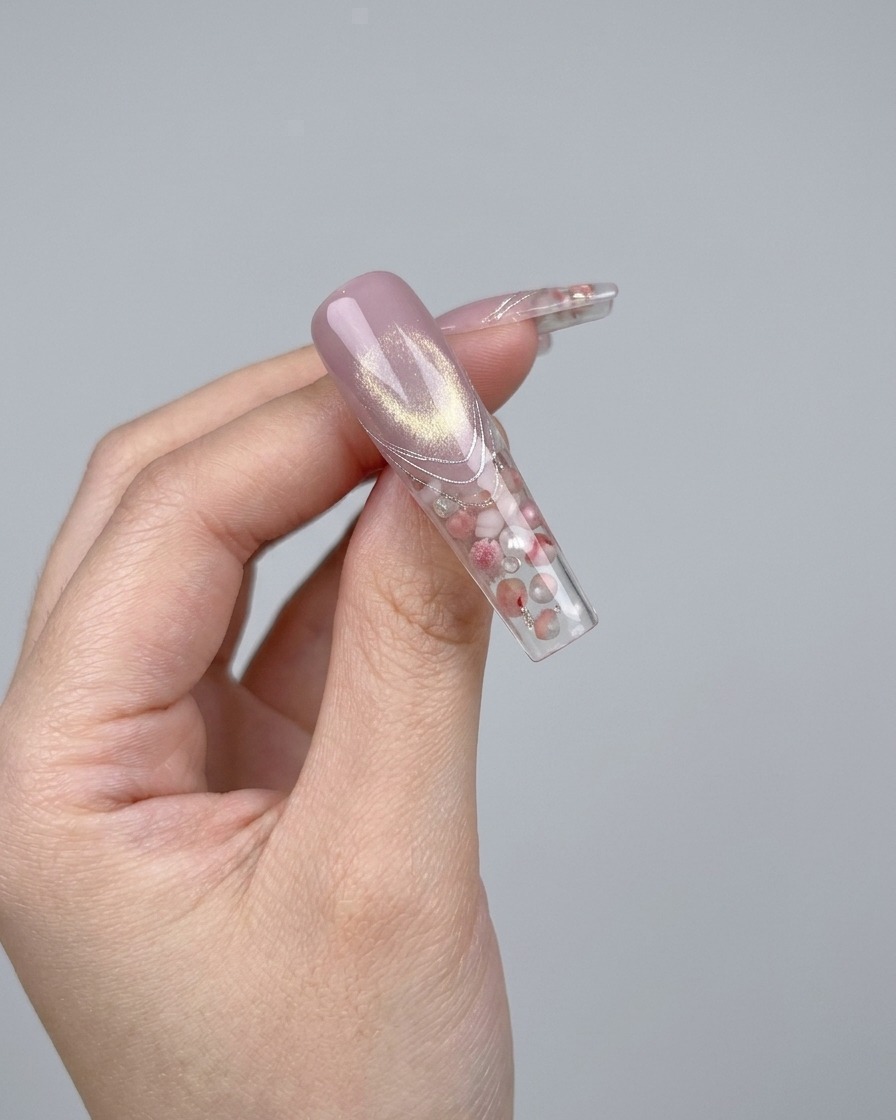 Un par de pinzas colocando un pequeño y brillante lazo de cristal 3D sobre una uña.