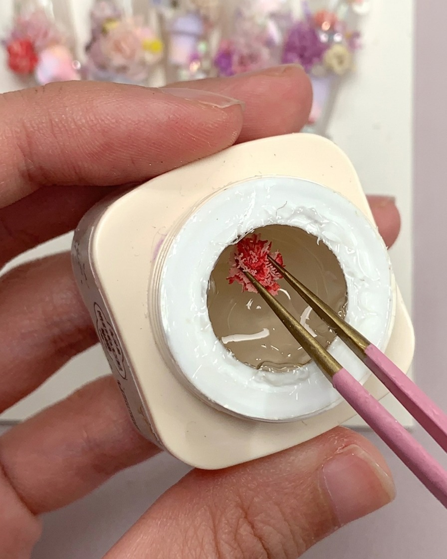 Un pincel aplicando una gota de pegamento de gel escarchado sobre un tip de uña de plástico transparente.