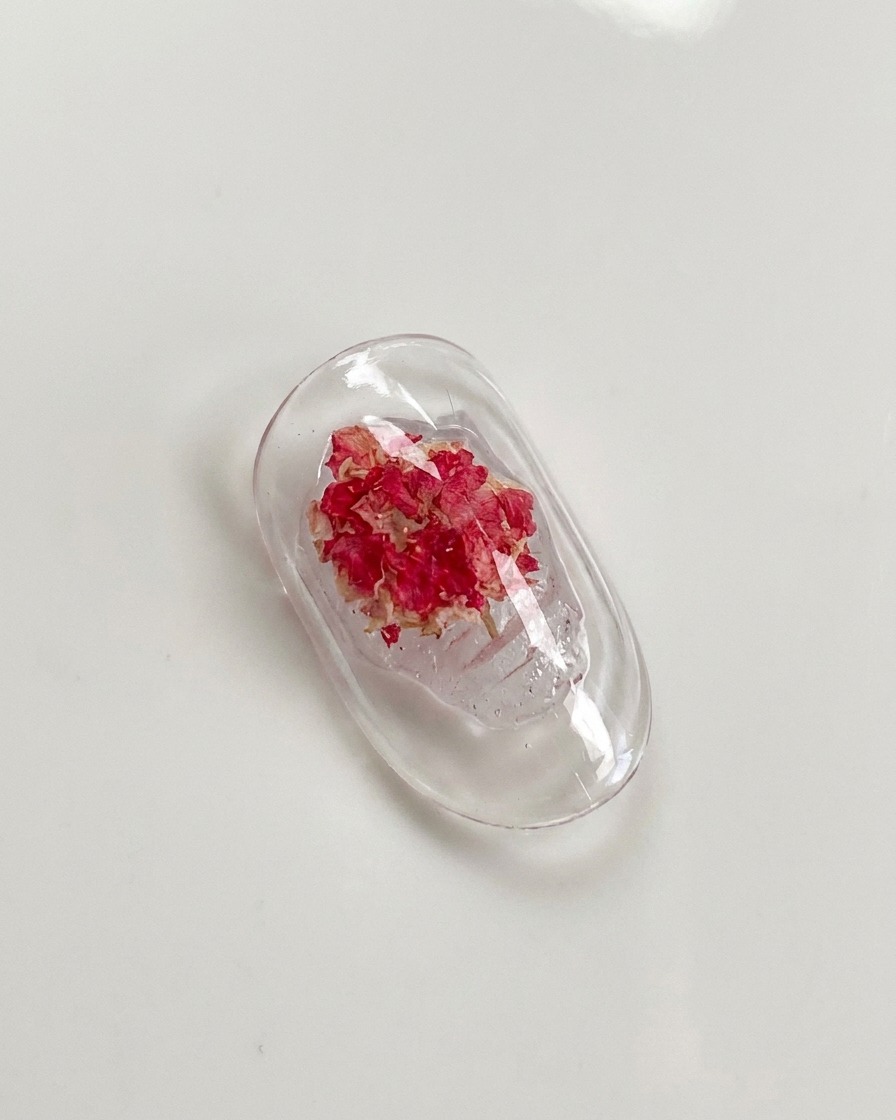 Un pincel de detalle presionando suavemente sobre los pétalos de una rosa seca incrustada en gel de uñas.