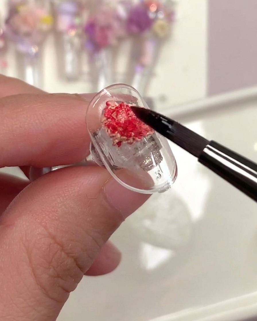 Un pincel aplicando un top coat transparente sobre una rosa seca en una uña.
