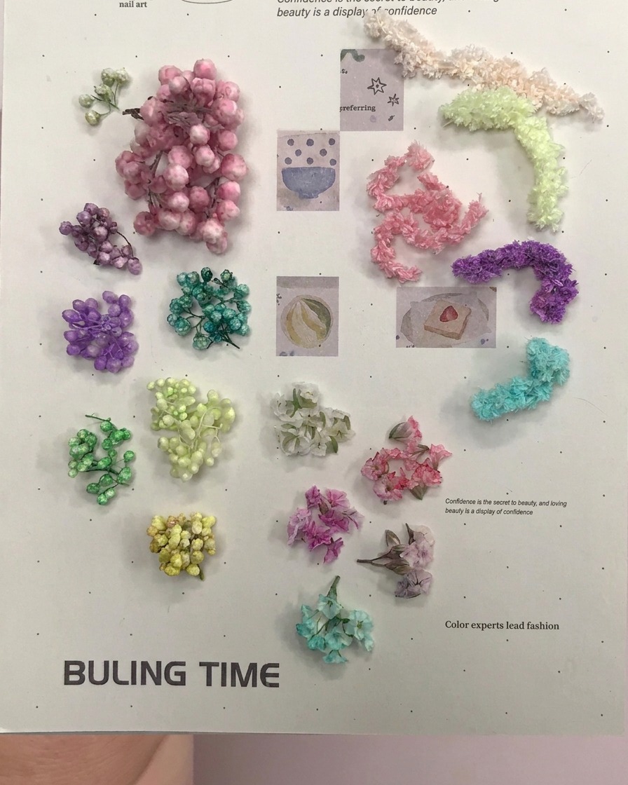 Un par de pinzas doradas recogiendo pequeñas bolas florales secas moradas de una superficie plana.