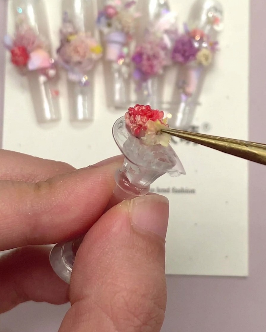 Un par de pinzas sosteniendo un pequeño adorno de uña floral después de haber sido encapsulado.