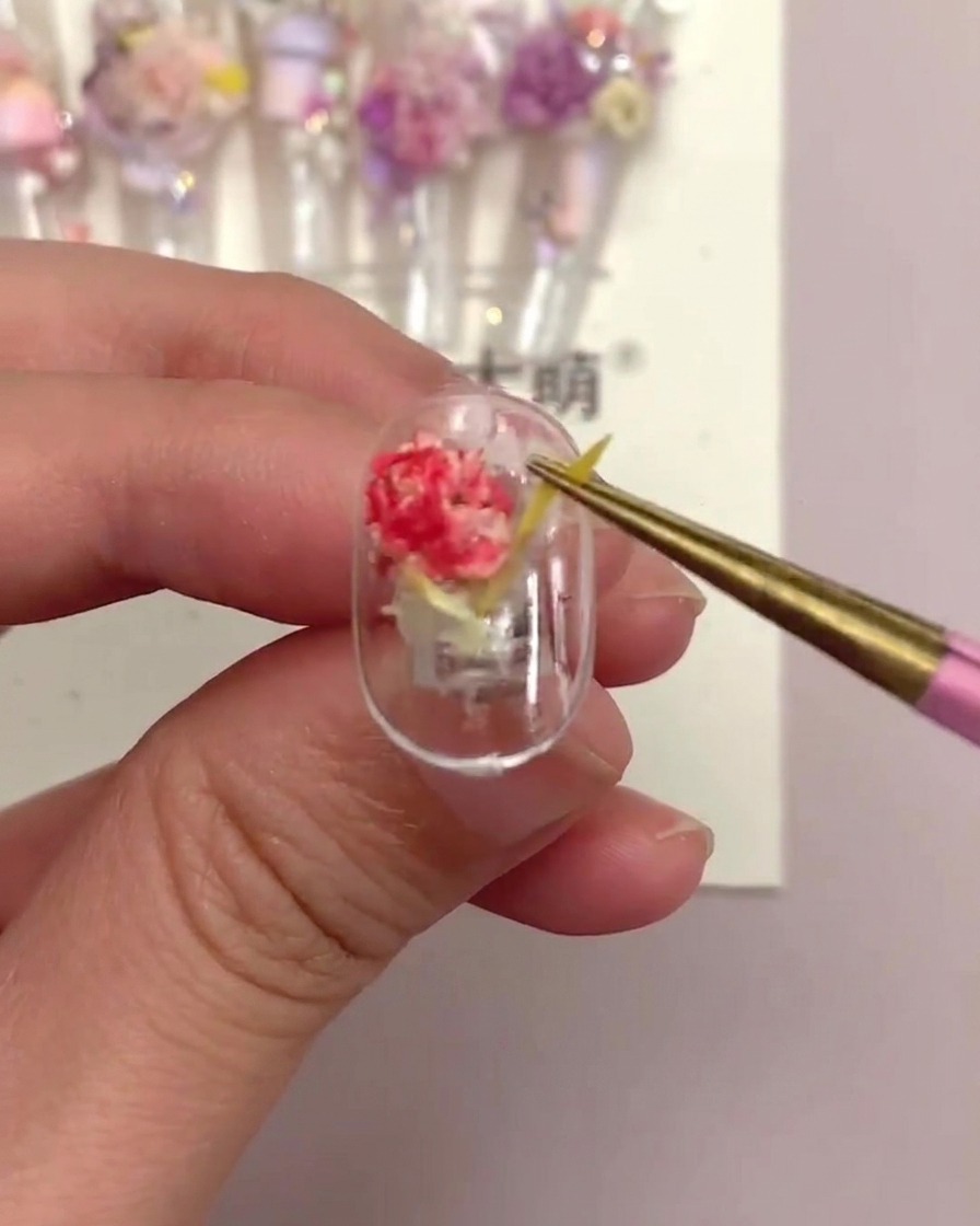 Un par de pinzas tirando suavemente de una pieza floral lineal amarilla en un tip de uña terminado para probar su seguridad.