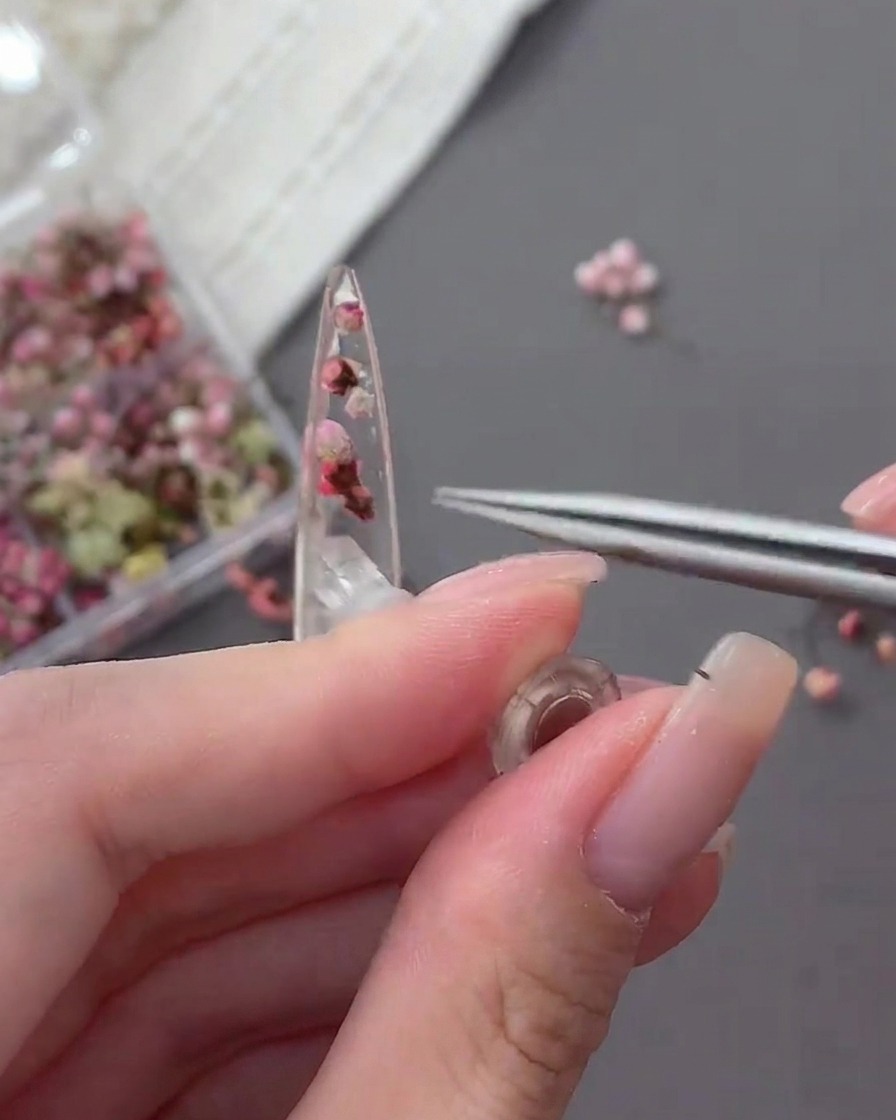 Primer plano de unas pinzas colocando un pequeño strass transparente sobre el gel húmedo.
