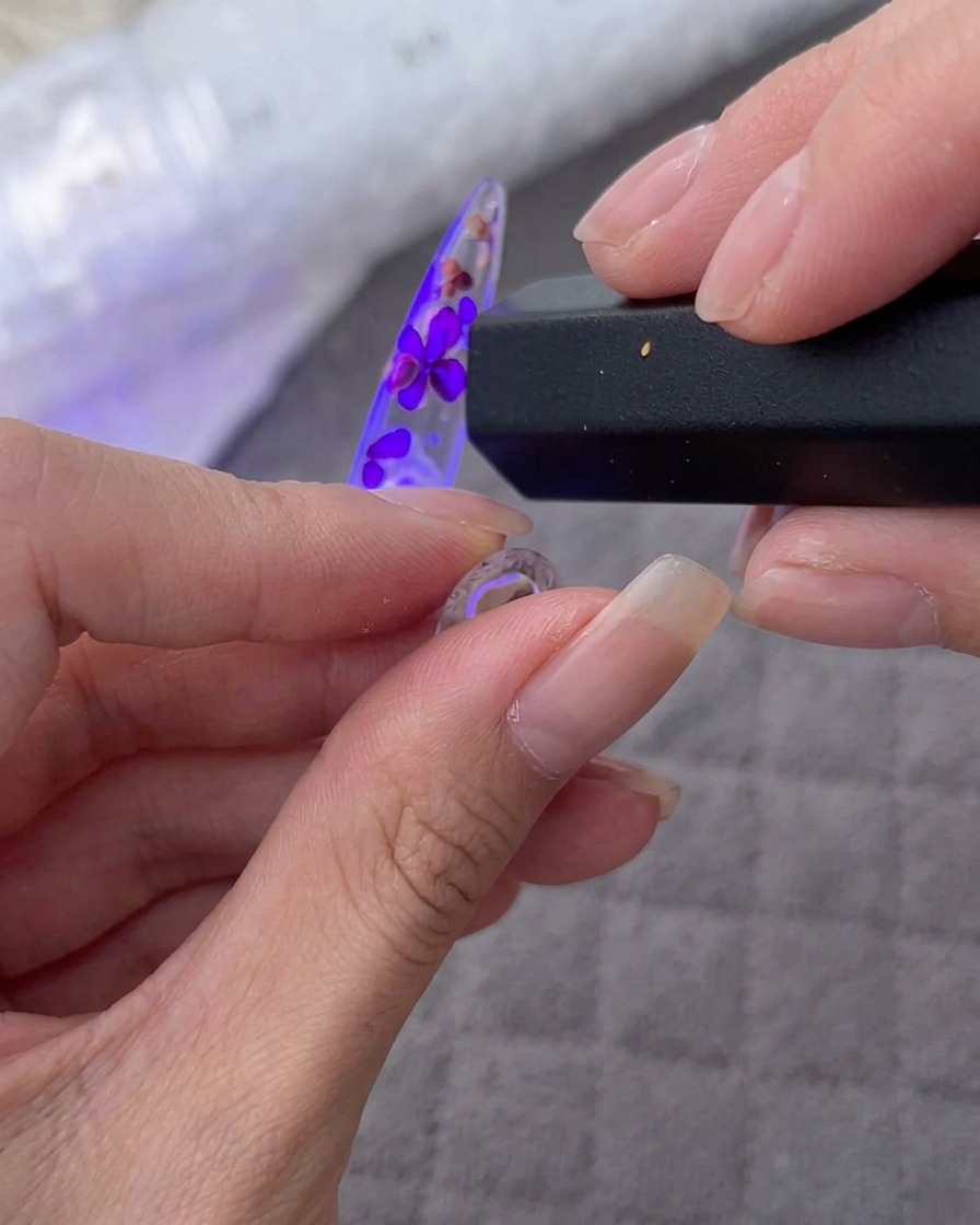 Mano sosteniendo una lámpara UV/LED sobre la punta decorada con flores y cristales.