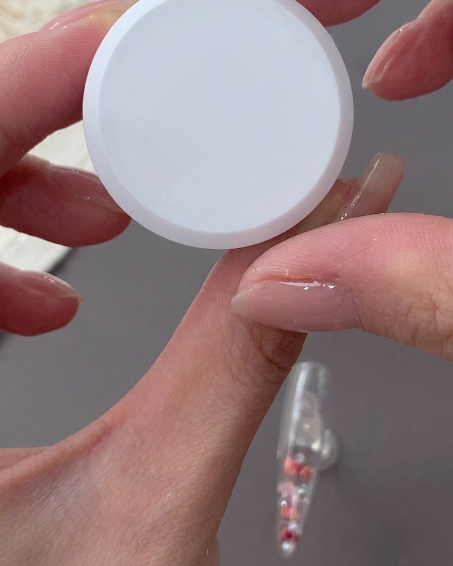 Mano usando una esponja para aplicar gel blanco lechoso en el borde de la uña.