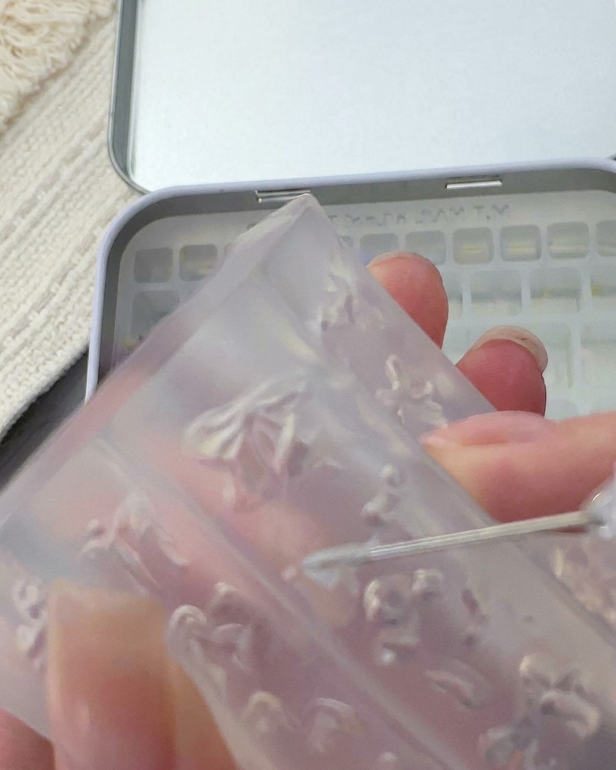 Herramienta metálica levantando un lazo 3D blanco de un molde de silicona.