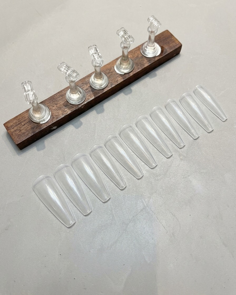 Primer plano de una mano utilizando una lima para pulir suavemente la superficie de una punta de uña artificial transparente.