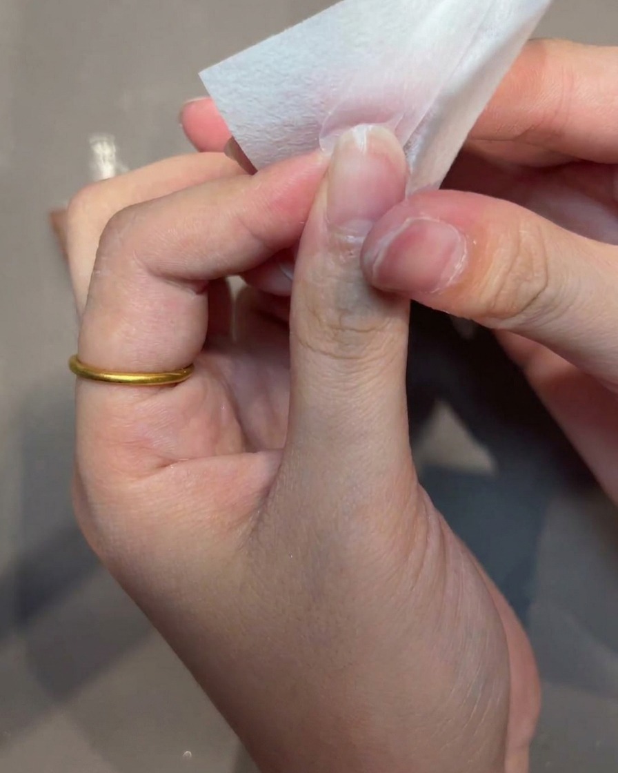 Primer plano de una mano utilizando una toallita sin pelusa para limpiar la superficie de una punta de uña.