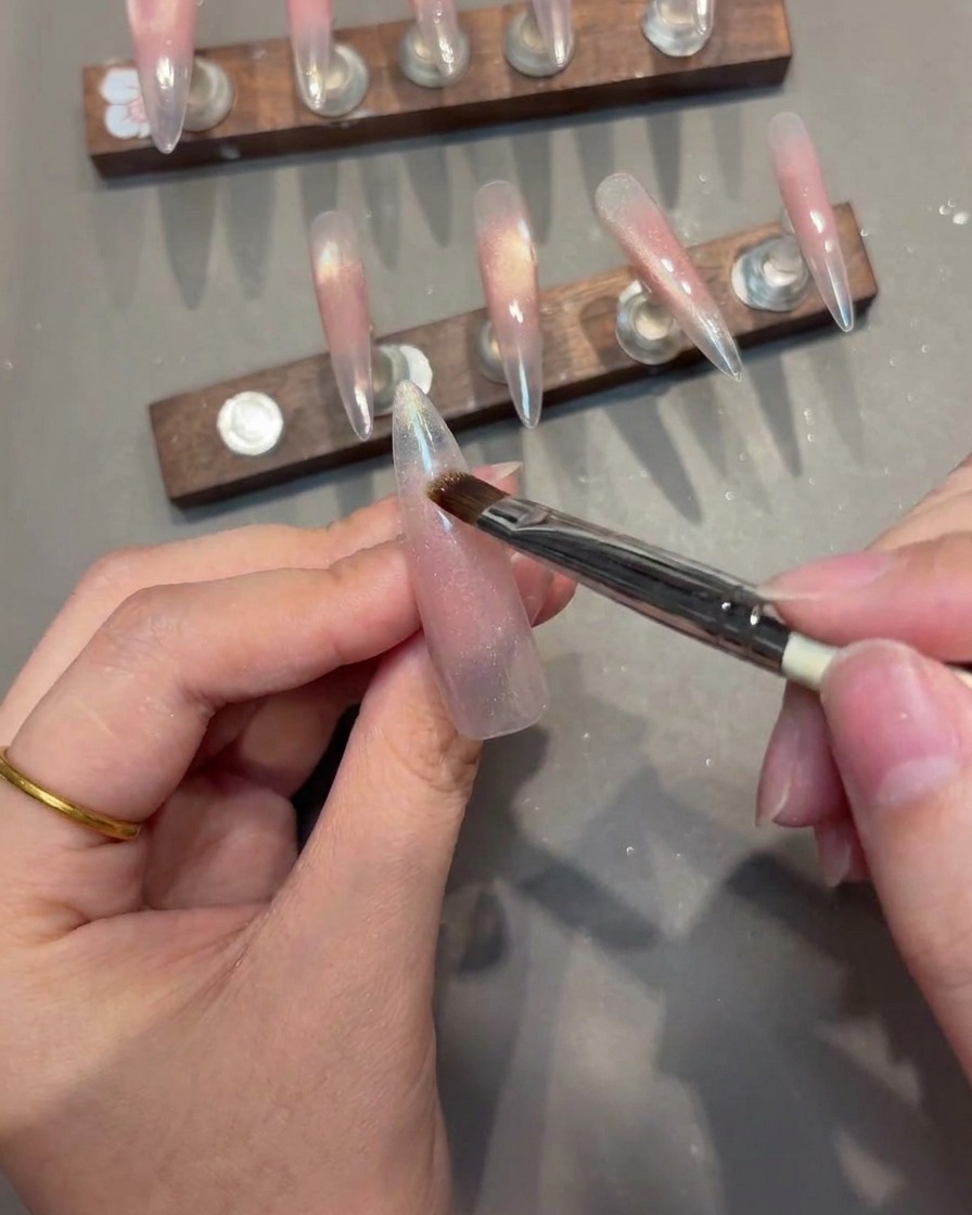 Primer plano de un pincel aplicando gel magnético en una uña, con el imán posicionado para crear una línea en V.