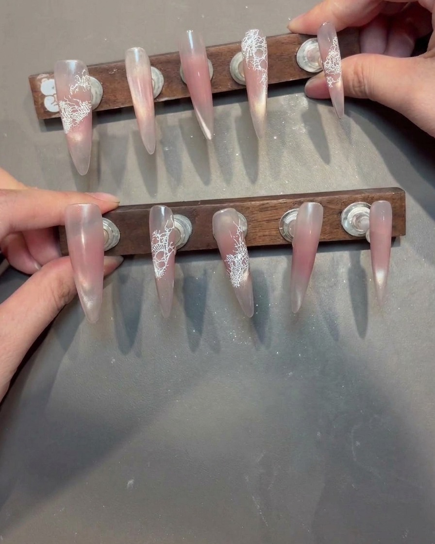 Un pincel aplicando un gel de refuerzo transparente sobre una uña con un patrón de encaje blanco.