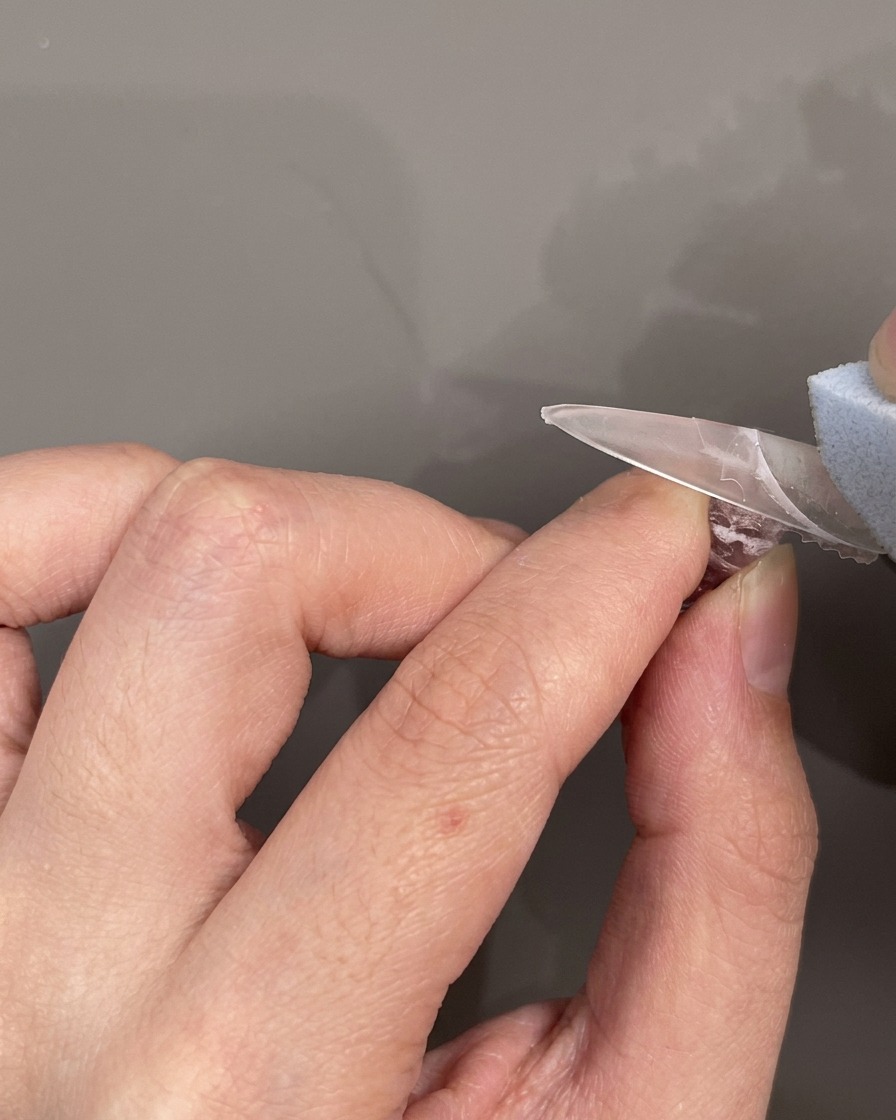 Una pegatina de silicona para línea de sonrisa francesa colocada horizontalmente sobre una uña para enmascarar el área de la punta.