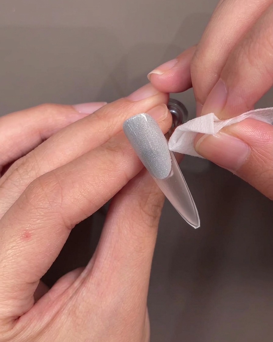Pinzas levantando una guía de silicona de línea de sonrisa de una uña, revelando un borde limpio y curvo en el gel azul.