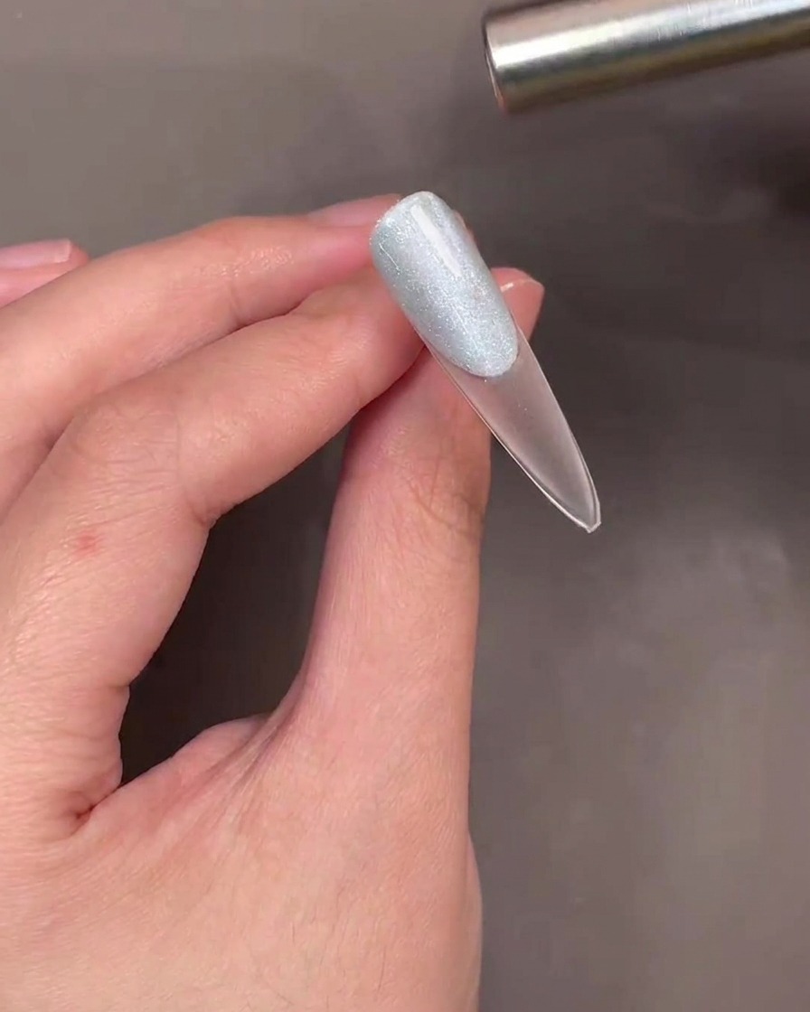 Una varita magnética sostenida sobre una uña con gel cat-eye azul para crear un efecto de brillo.