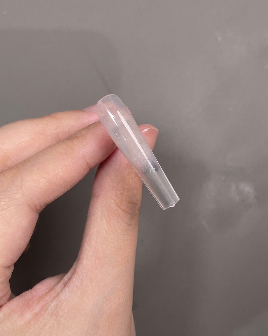 Una herramienta de silicona azul aplicando gel de textura blanca horizontalmente a través del centro de un tip de uña.