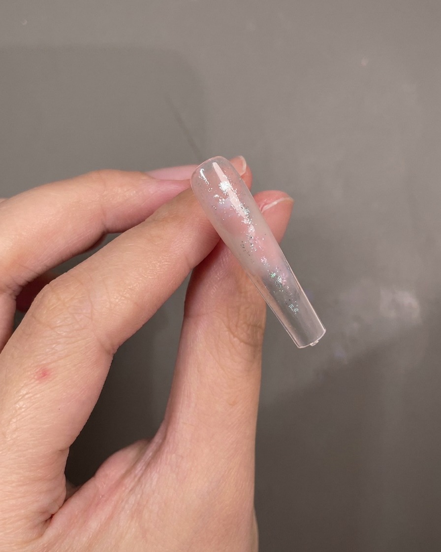 Un pincel dando toques de gel cat-eye azul sobre un tip de uña pintado de forma abstracta.