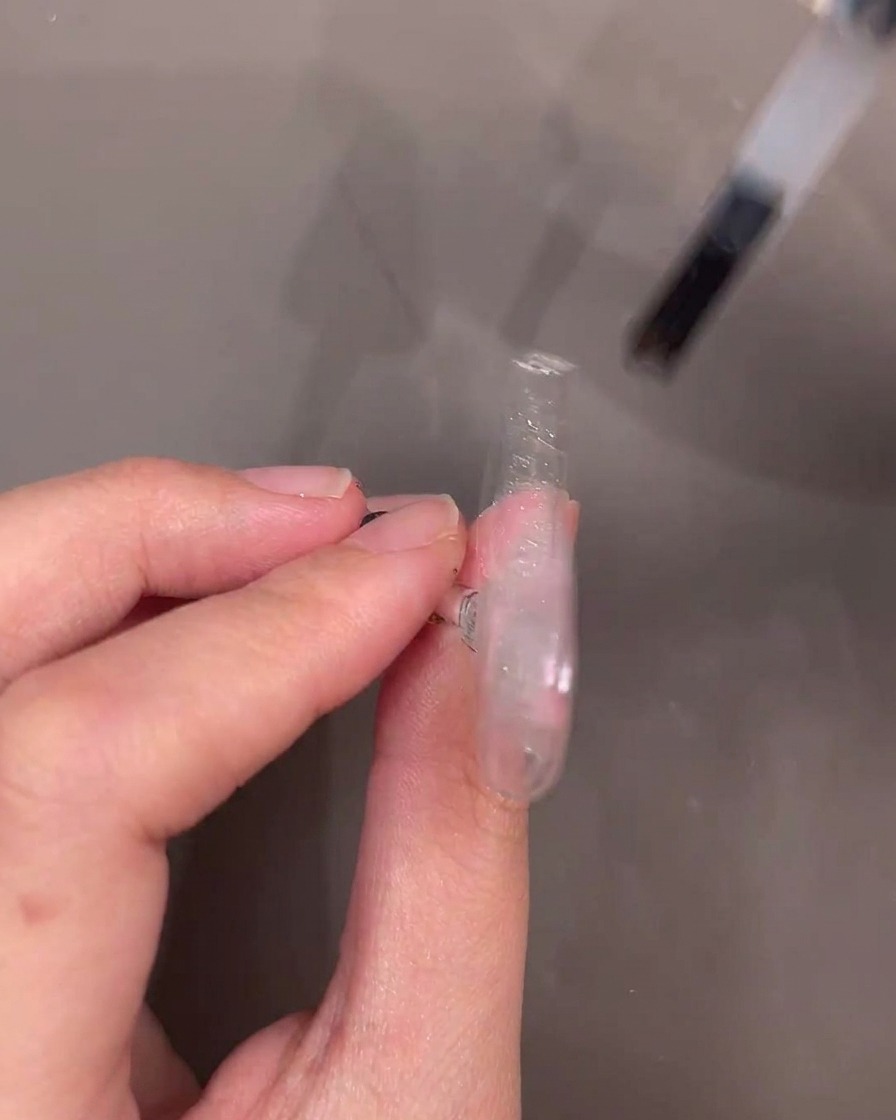 Un pincel de esmalte de gel aplicando una capa de gel de refuerzo transparente sobre un tip de uña decorado.