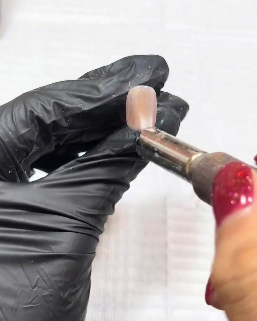 Primer plano de un imán siendo utilizado sobre una uña para manipular las partículas ojo de gato en una gota central definida.