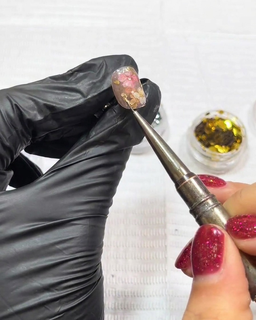 Primer plano de pinzas colocando un pequeño charm de estrella metálica sobre una uña decorada.