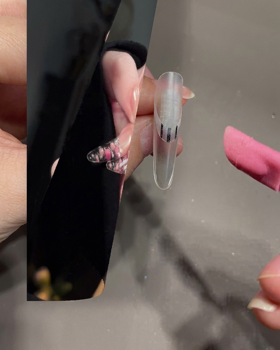 Un pincel para decoración de uñas extendiendo gel blanco sobre la punta de una uña transparente.