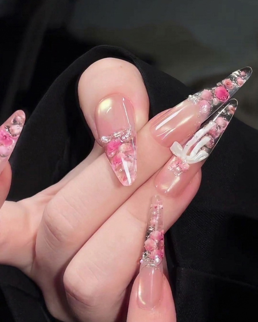 Un pincel de precisión colocando pequeñas perlas blancas y diamantes de imitación sobre el diseño floral en la parte trasera de la uña.